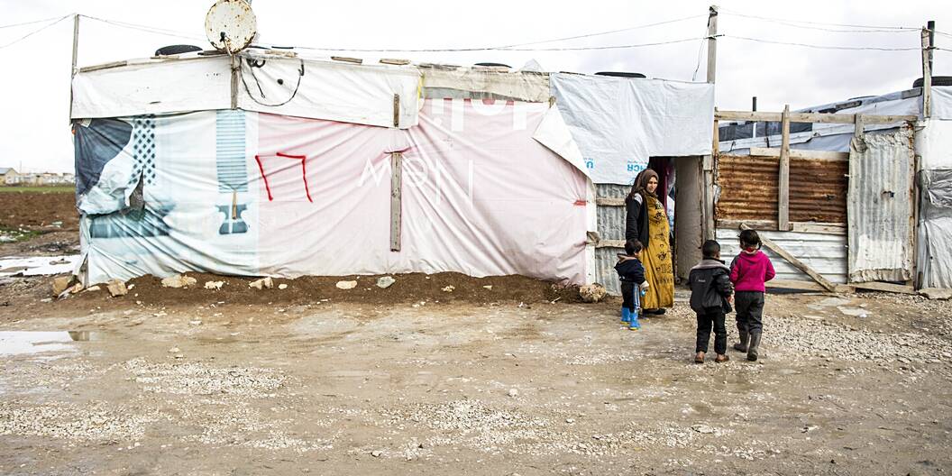Eine Mutter steht mit ihren drei Kindern vor dem Eingang ihrer Unterkunft in einem Flüchtlingslager im Libanon.